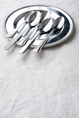 Vintage weathered silver metal spoon in pattern form on round shape silver plate on white fabric table top background with empty copy space for text