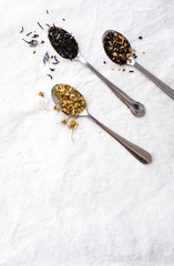 Different types of tea on vintage metal silver spoons on white fabric background with empty copy space. Organic healthy lifestyle and well-being concept. Vintage food and drink setting styling. 