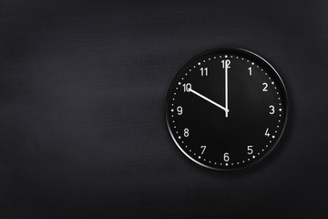 Black wall clock showing ten o'clock on black chalkboard background. Office clock showing 10am or...