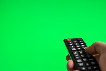 Male hand with TV remote control over green screen. Place for your advertisement.