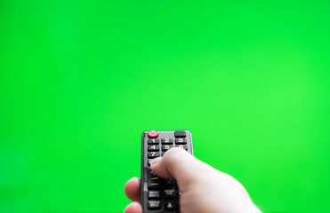 Male hand with TV remote control over green screen. Place for your advertisement.