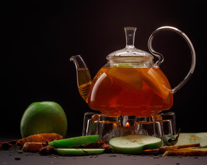 Amber-colored apple tea and apples on a black background
