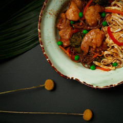 a plate wok noodles with chicken on a gray background green leafs yellow dried flowers craspedia Globosa