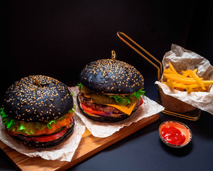 two juicy black burger with crispy fries served in a restaurant on a black background