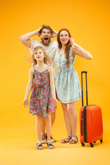 Happy surprised parent with daughter and suitcase at studio isolated on yellow background. Travel, vacation, parenthood, togetherness, tourism concept.