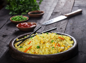 Cooked rice with curry and vegetables in a pan with chopsticks on the wood black background.