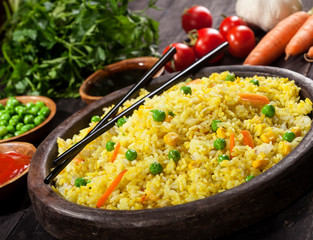 Cooked rice with curry and vegetables in a pan with chopsticks on the wood black background.