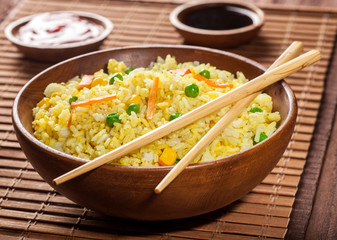 Cooked rice with curry and vegetables in a bowl with sauces and chopsticks on the wood brown bamboo background.