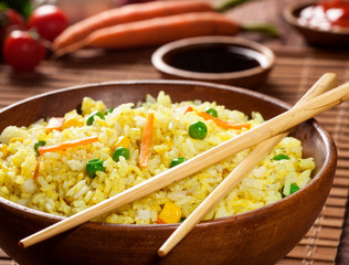 Cooked rice with curry and vegetables in a bowl with sauces and chopsticks on the wood brown bamboo background.