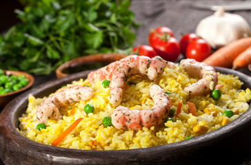 Cooked rice with shrimps, curry and vegetables in a dish on the wood black bamboo background.