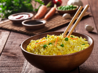 Cooked rice with curry and vegetables in a bowl with sauces and chopsticks on the wood brown background.