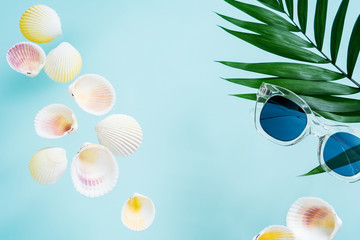 Fototapeta na wymiar Summer creative concept. Minimal style with transparent sunglasses, palm leaves and seashells on turquoise background with copy space
