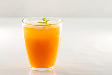 An inviting glass full of orange juice with a fresh mint leaf that floats on white white background