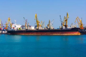 Bulk carrier ship in the port on loading. Bulk cargo ship under port crane bridge. Panorama of the...