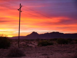 Naklejka na ściany i meble Sunset sky of orange and yellow in the vast Karoo of South Africa. With silhouette of telephone pole and wires leading to mountain range