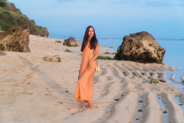 Attractive girl in sundress with bag on long strap and sunglasses posing on tropical beach