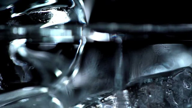 selective focus of clear water pouring into transparent glass with ice cubes isolated on black