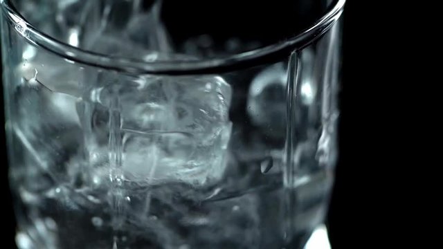close up view of clear water pouring into transparent glass with ice cubes isolated on black