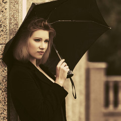 Sad young fashion woman with umbrella on city street