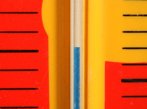 Close up image of a liquid in glass thermometer with a bright yellow and red background