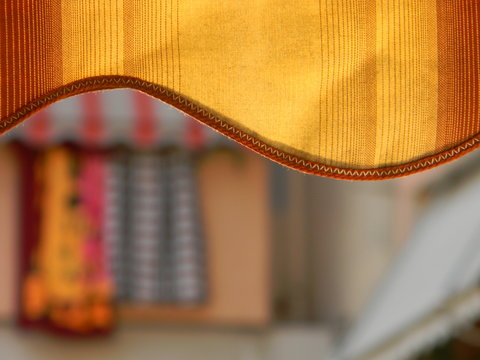 Close up view of a yellow awning with the blurred image of striped awning and colorful laundry in the background (bokeh) 