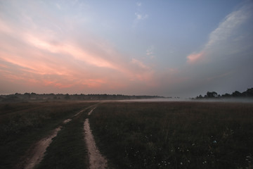 Sunrise on the fields with fog, rural road.