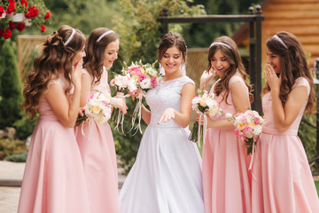 Happy bride with bridesmaid hold bouquets and have fun outside. Beautiful bridesmaid in same...