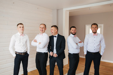 Handsome groom with his groomsman at home. Five man. Groom dressed in suit, gromsmen in white shirt. Funny guys on the wedding