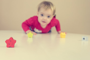 Cute blonde girl wearing red dress playing with toys at the table.