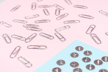 Metal push pins and paper clips scattered on blue and pink sheets of paper