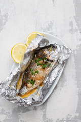baked fish with lemon in aluminium foil on ceramic background