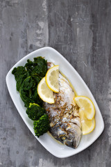 baked fish with lemon in white dish on ceramic background