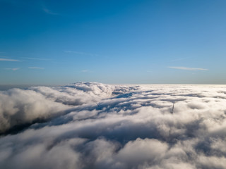View of a drone above the fog, wind turbines with fog and blue sky