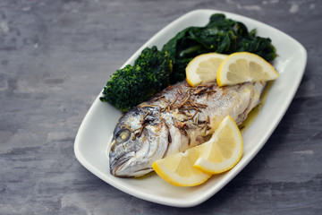 baked fish with lemon in white dish on ceramic background