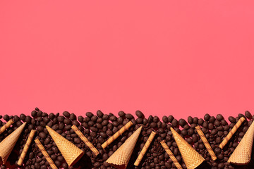 Chocolate dragee and waffle cones placed in fascinating order on coral background, view from above