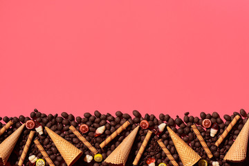 Chocolate dragee and waffle cones placed in fascinating order on coral background, view from above