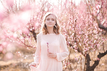 Blonde girl 16-17 year old walking in peach orchard. Looking at camera. Spring season.