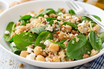 Healthy salad with spinach, chickpeas, quinoa, feta cheese and walnuts in white plate on concrete background. Selective focus.