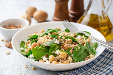 Healthy salad with spinach, chickpeas, quinoa, feta cheese and walnuts in white plate on concrete background. Selective focus.