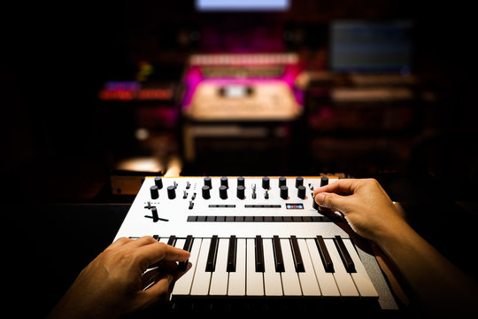 musician, producer, composer, arranger hands playing keyboard synthesizer in recording studio, music production concept