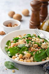 Healthy salad with spinach, chickpeas, quinoa, feta cheese and walnuts in white plate on concrete background. Selective focus.