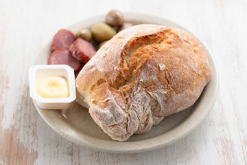 bread with butter, olives and smoked sausage on dish on wooden background
