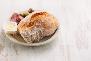 bread with butter, olives and smoked sausage on dish on wooden background
