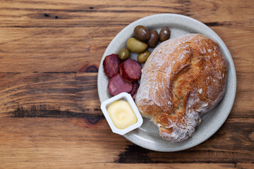 bread with butter, olives and smoked sausage on dish on wooden background