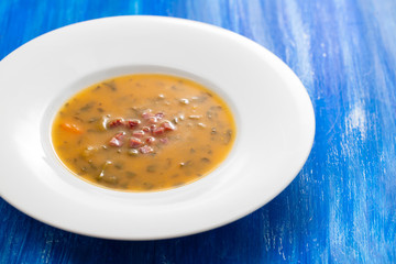 soup with smoked meat in white plate on wooden background
