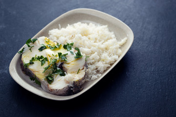 boiled perch with parsley and boiled rice on dish on ceramic background