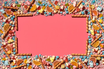 Multicolored glazed dragees and other sweets are arranged in the form of a frame on a coral...