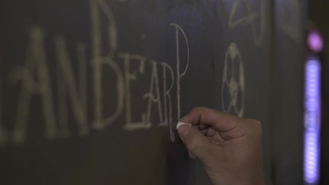 Male hand drawing chalk on black board beer menu in bar pub. Waiter writing menu on chalk board in restaurant. Drawing price in brewery bar.
