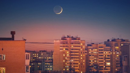 Beautiful waxing crescent moon setting behind city skyline buildings rooftops at night. Zoom in. Timelapse, 4K UHD.