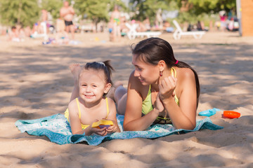 Little girl with mom playing with sand on the beach